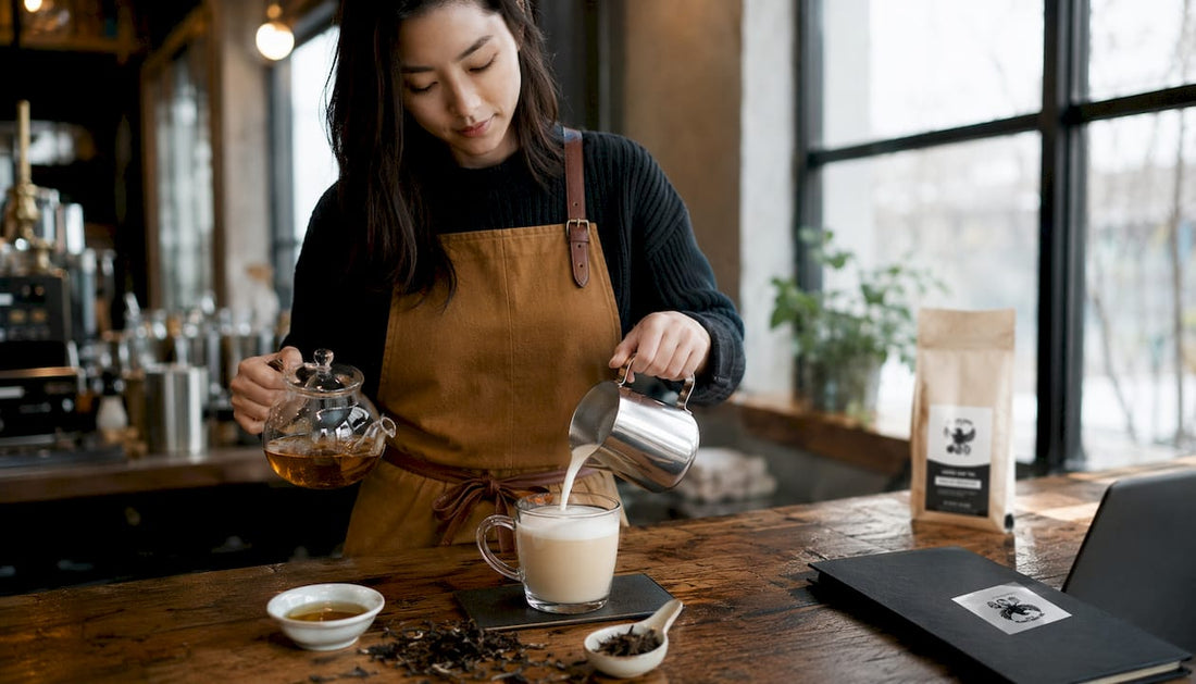 Woman pouring steamed milk to tea latte in kitchen