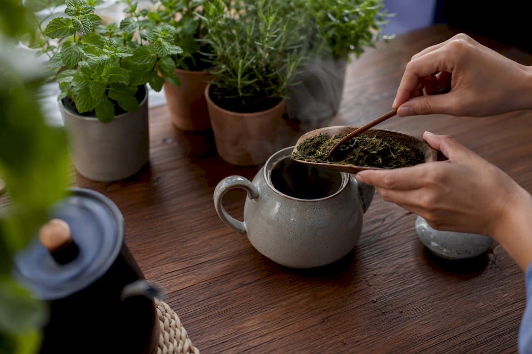 Hands pouring water into teapot with loose leaf tea