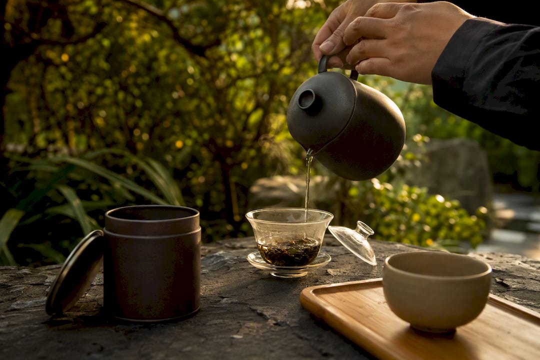 Hands pouring hot water over tea leaves in gaiwan