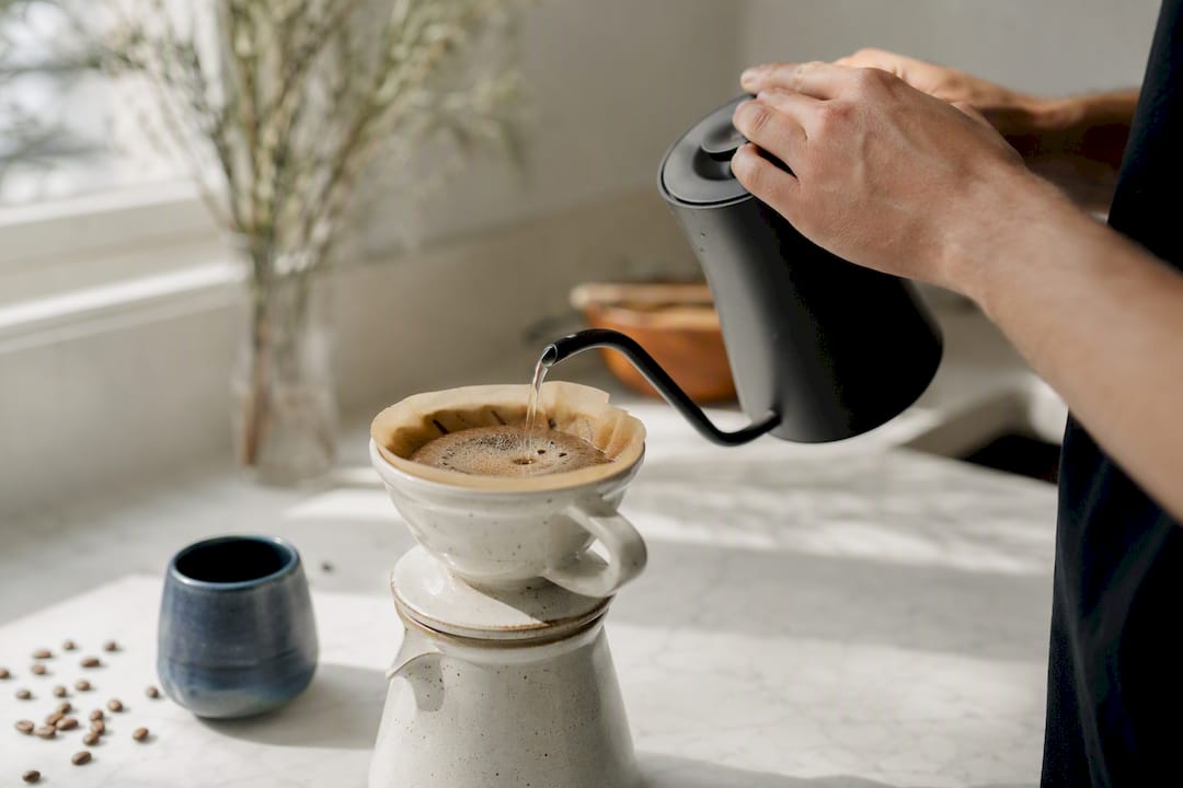 Hands pouring hot water over coffee grounds