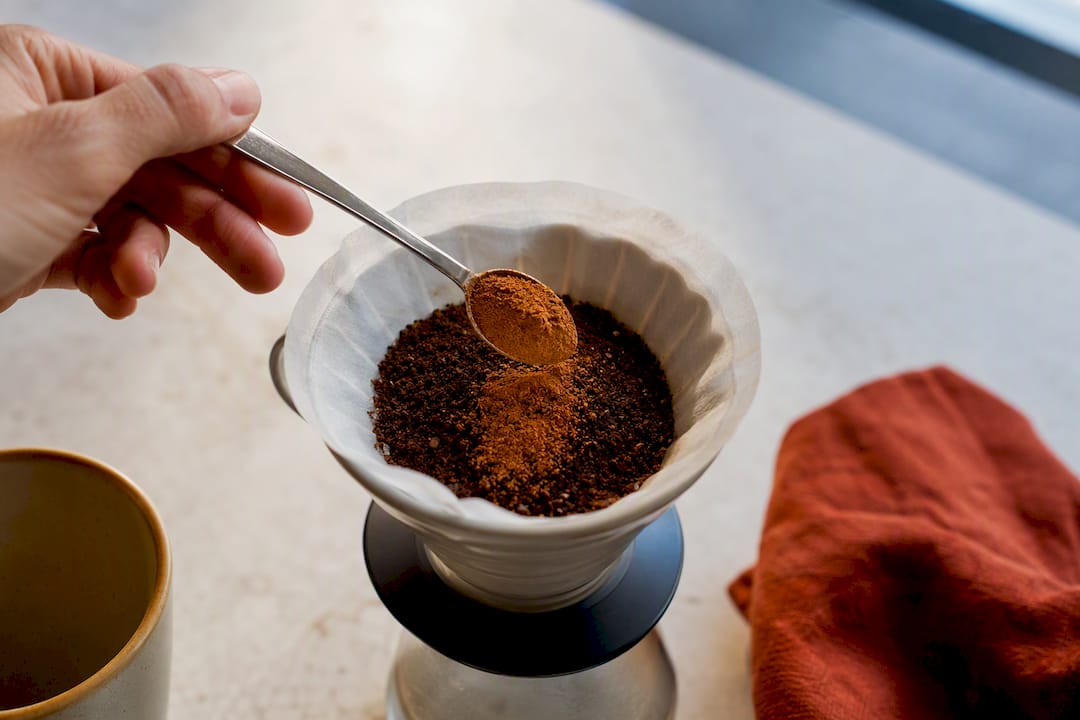 Hand mixing cinnamon into coffee grounds